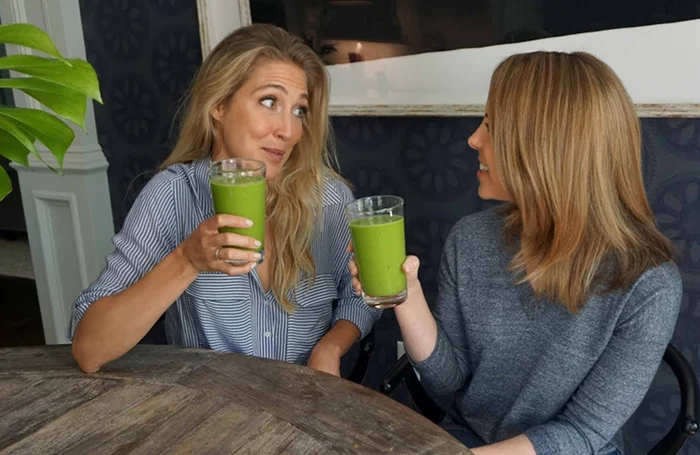 Two beautiful women sitting at a table and drinking smoothi ​​with youtube video capture