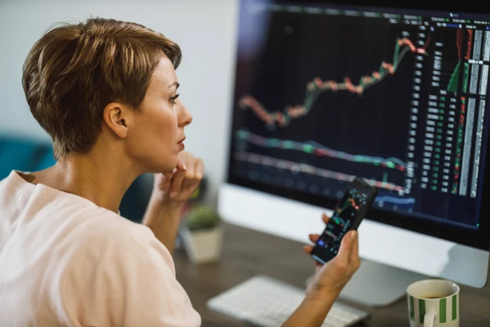 A woman looks at some bursa graphics on a monitor and on the phone