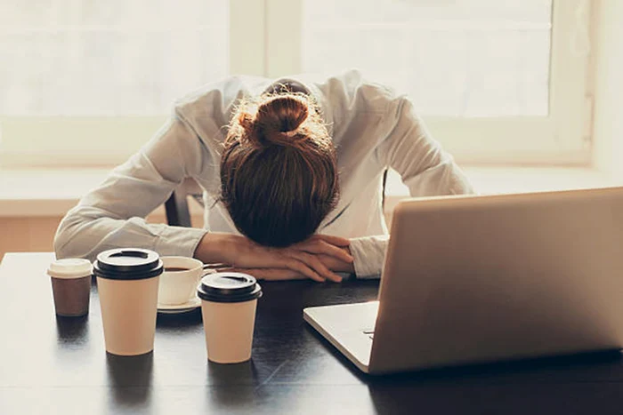 A woman sleeping at the office with more than one glasses of coffee source Istock