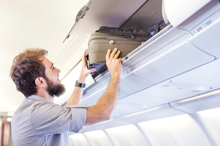A man who puts a suitcase in the compartment above the shutterstock photo plane seats