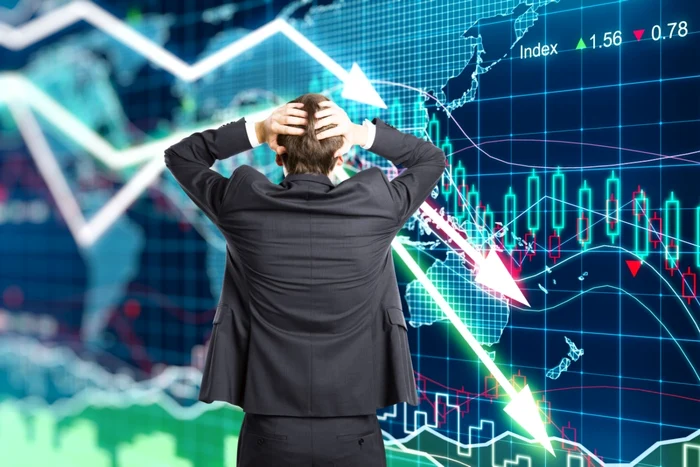 A businessman holds his hands on his head, worriedly looking at the graphs that indicate decrease
