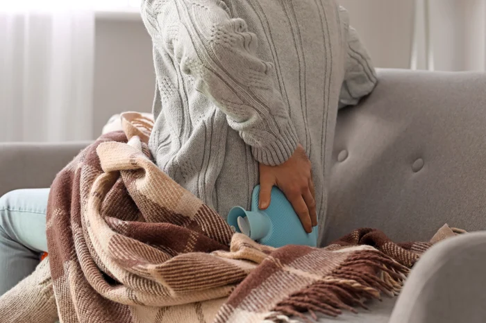 Person that relieves lumbar pain with a bottle of hot water shutterstock
