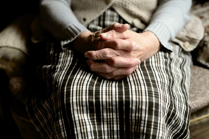 Old man with hands together, sitting on a shabby armchair