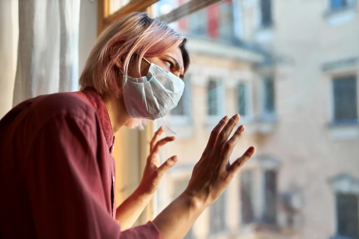 A sick woman of Covid, wearing his mouth mask, looked up angry on the window