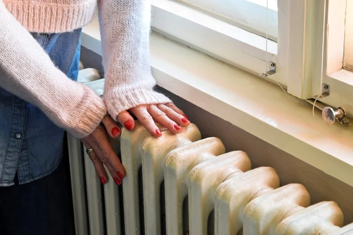 A woman keeps her hands on the cold radiator, trying to find out if the heat will turn back on