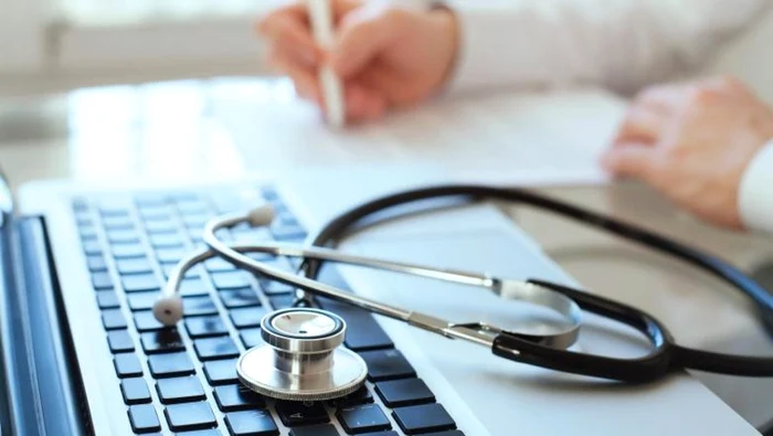 Doctor writing a prescription in medical office with stethoscope left on laptop keyboard