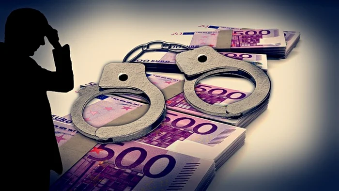 Shadow of a man holding his hand to his forehead while looking at handcuffs on stacks of euros