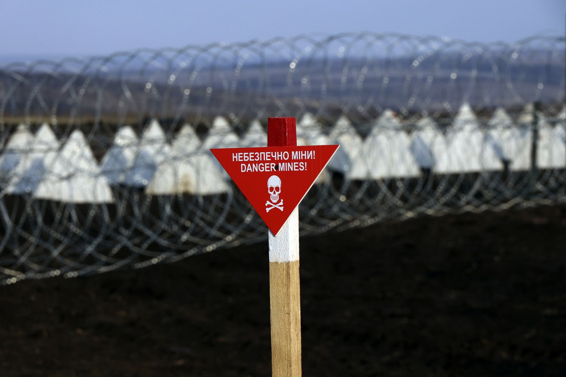 Sign "Warning: mines!" in front of barbed wire lines in a field in the Kharkiv region. Ukraine, March 29, 2025