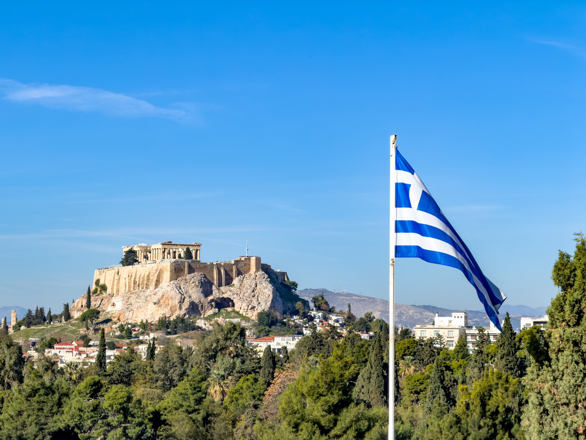 The Greek flag flying next to the Acropolis hill in Athens