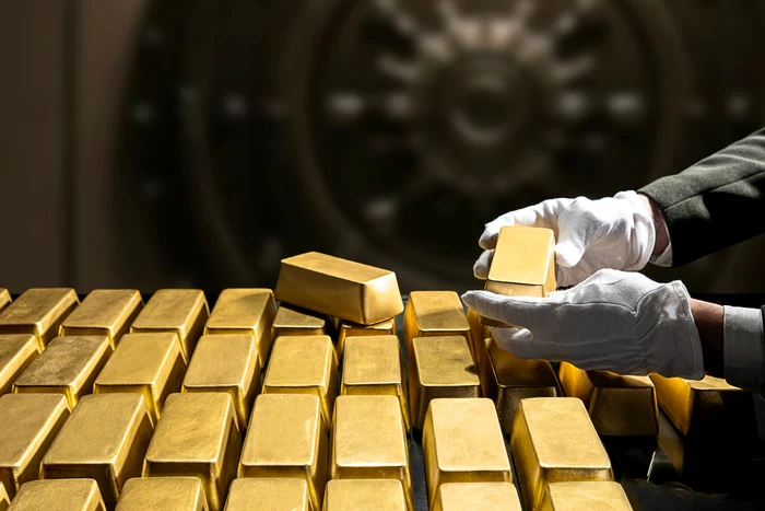 Someone is holding a gold bar next to many such pieces