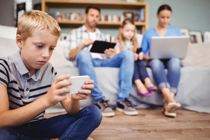 Parents with two children sitting in the living room, all eyes on laptops, phones or tablets