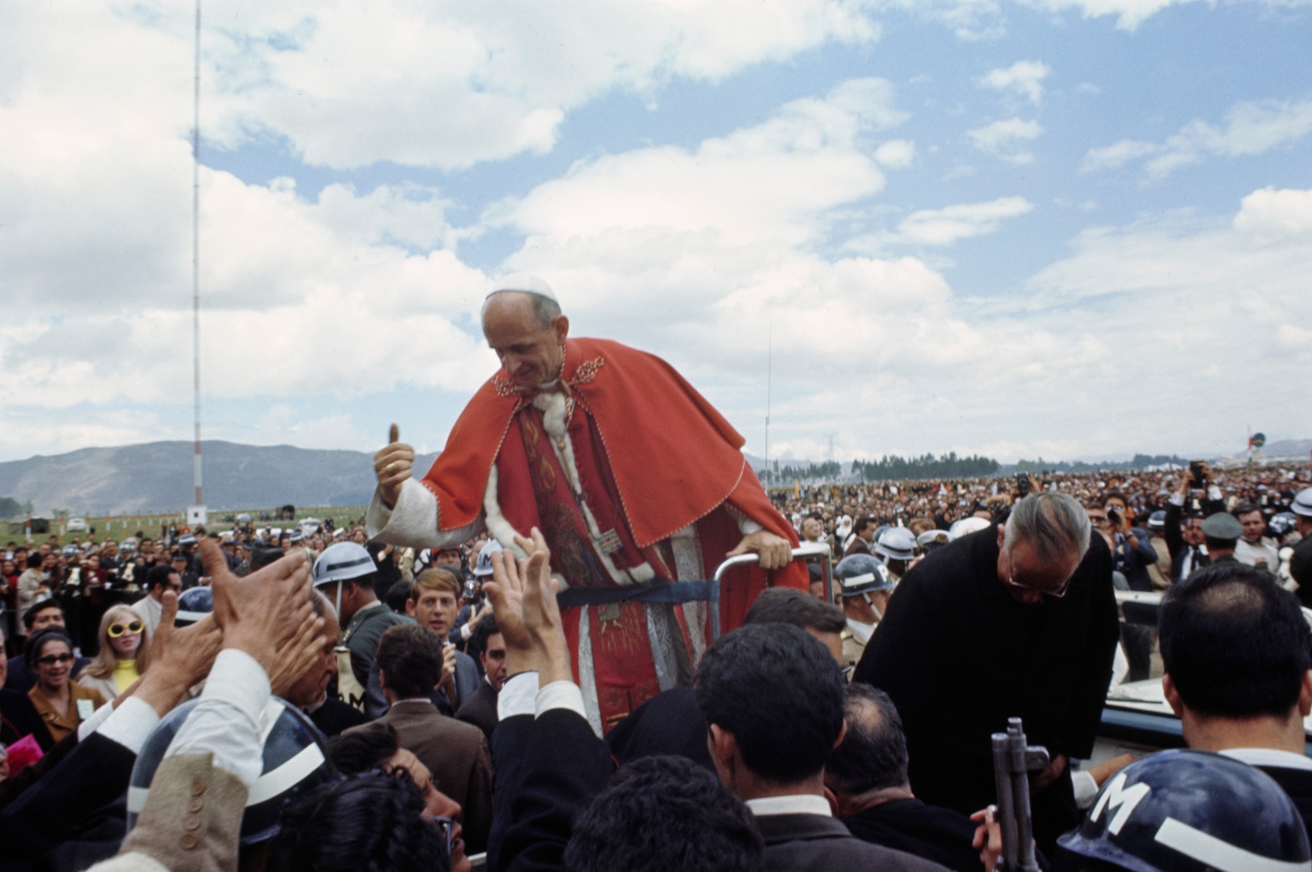 Surrounded by military police and bodyguards, Pope Paul VI waves to the crowd from the backseat of a car during a 1968 visit to the suburbs of Bogotá, Colombia.